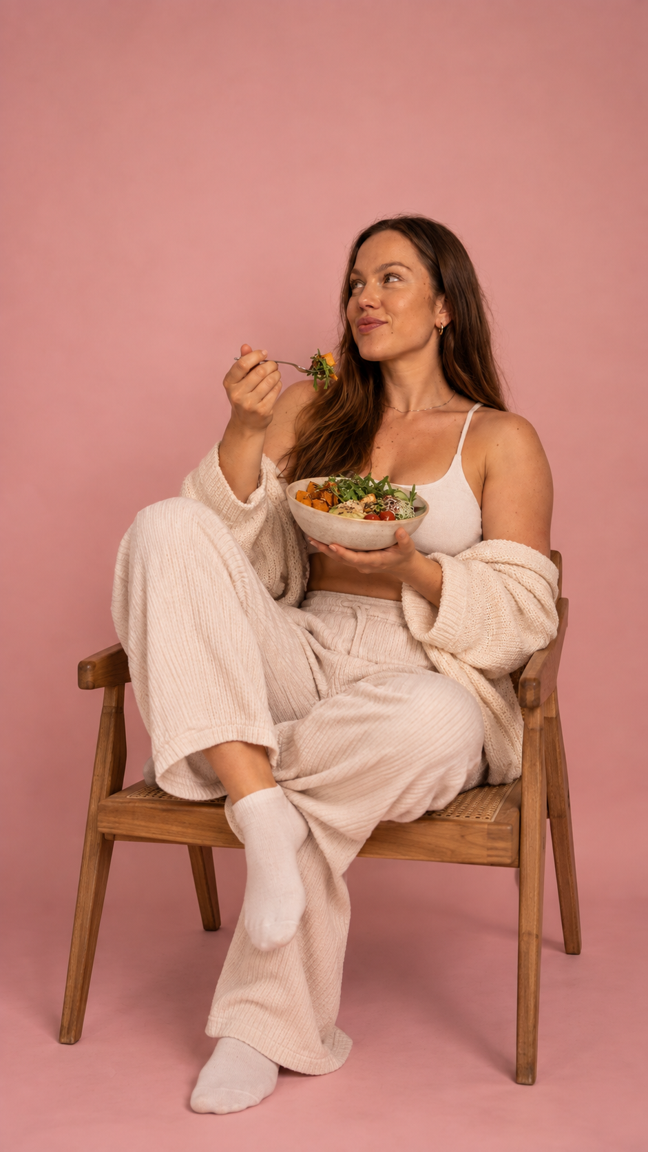 Rebecca sitzt mit einer Schale Essen in einem Holzstuhl